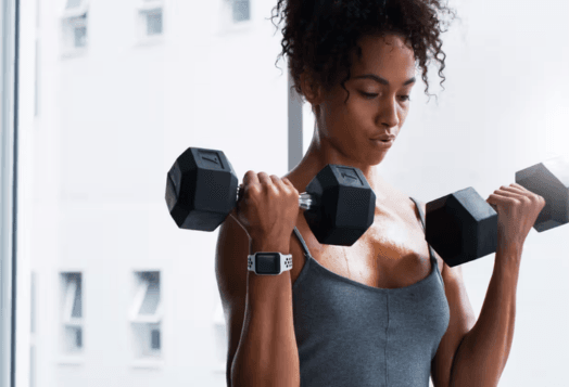 Woman lifting dumbbells, sweating, with a smartwatch