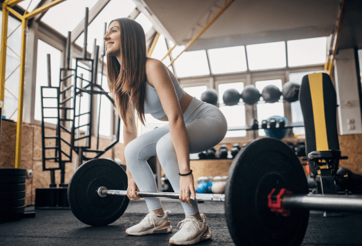 Woman smiling while deadlifting a barbell in a gym