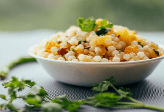 A bowl of Sabudana Khichdi, with cilantro and chilies on a dark background