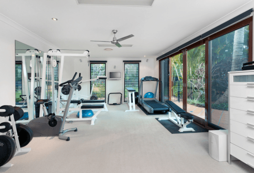 A bright, modern home gym with a treadmill, exercise bike, weights, and a mirror