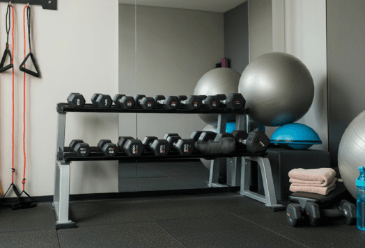 A home gym with a dumbbell rack, a large grey exercise ball, and resistance bands hanging on the wall