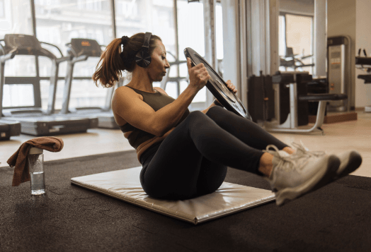 A woman in the gym doing Russian twists on a mat, holding a weight plate with both hands