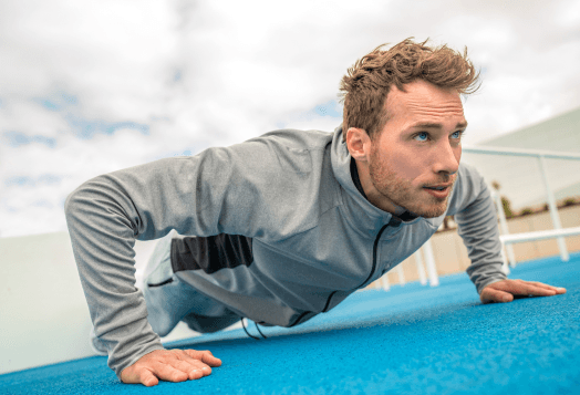 A low-angle shot of a man in a grey tracksuit doing a push-up on a blue outdoor surface