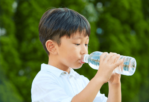 A boy in a white shirt drinking water from a plastic bottle