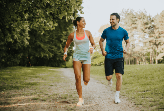 A man and a woman smiling while jogging on a path