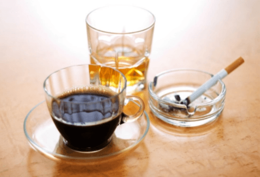 A cup of coffee, a glass of alcohol, and an ashtray with a cigarette