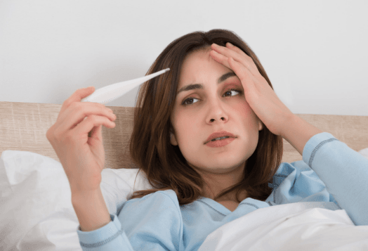 A woman in bed, with a thermometer, looking unwell