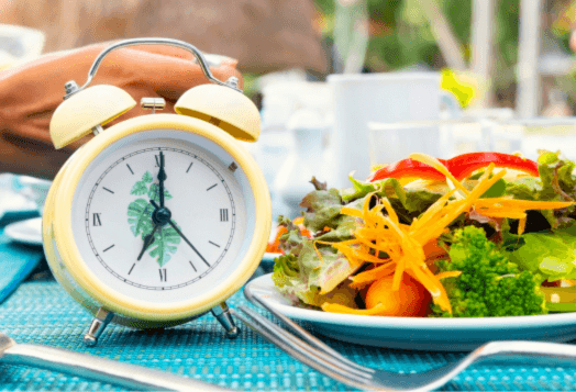An alarm clock next to a salad on a placemat