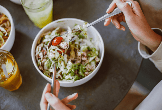 A person eating a fresh salad from a white bowl
