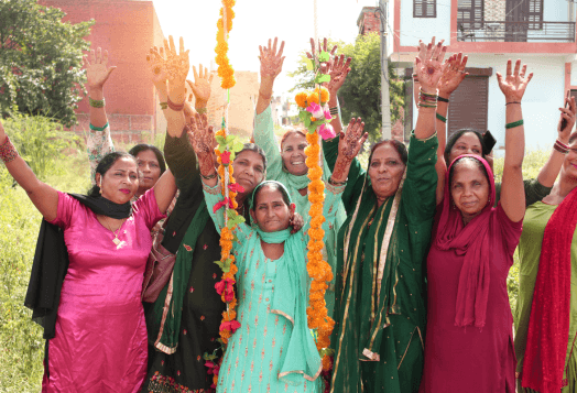 An excited group of women with henna-decorated hands raising their arms