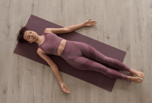  A woman lying on her back on a purple yoga mat, resting in a yoga pose