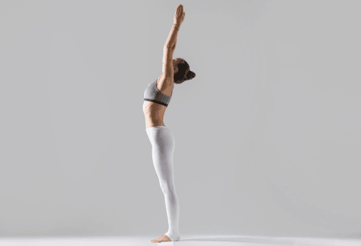 A woman in athletic wear performing a standing yoga pose with her arms raised