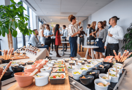 A crowded catered event with a table full of appetizers