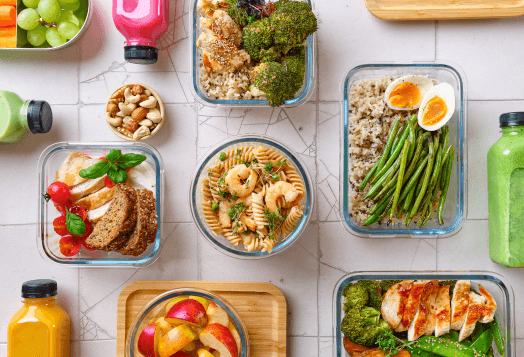An overhead shot of several glass meal prep containers filled with various healthy foods, including chicken, pasta with shrimp, and vegetables