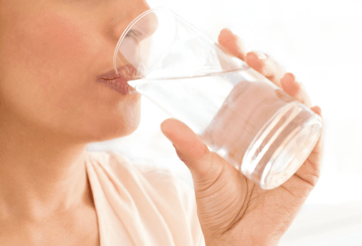 A close-up of a person's chin, mouth, and hand as they drink a glass of water