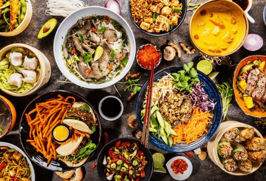 A high-angle shot of a table covered with a wide variety of Asian dishes, including noodles, soups, and spring rolls