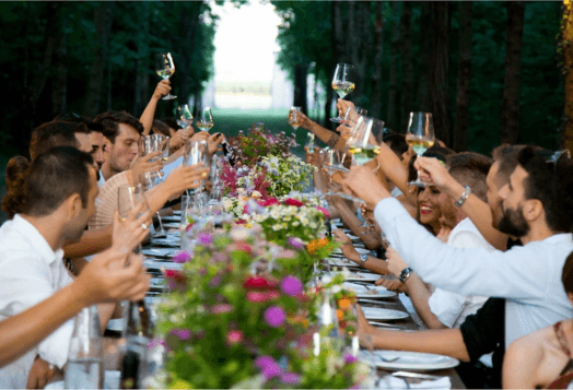 A dinner party in a garden, with people raising their glasses for a toast