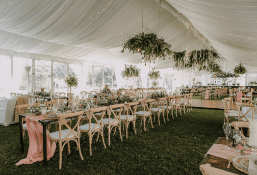 A decorated wedding tent with long tables and chairs on a grassy floor