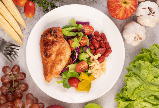 A top-down view of a plate with grilled chicken breast and a salad made of leafy greens, tomatoes, kidney beans, and other vegetables