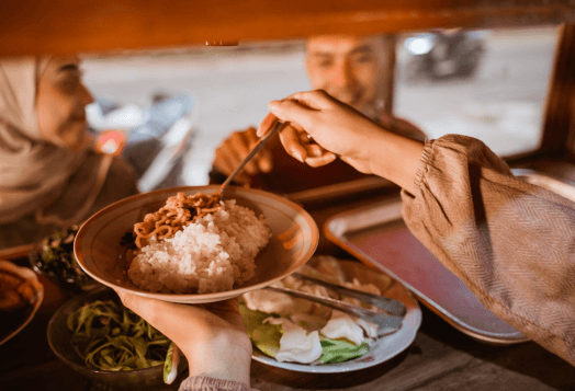 A hand serving rice and meat onto a plate