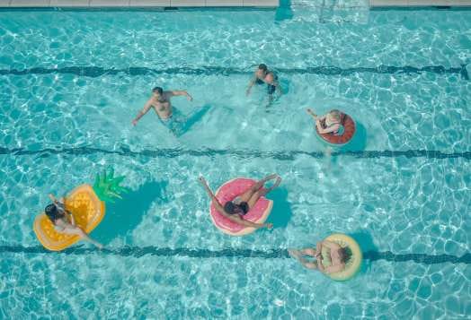 An aerial view of six people relaxing in a swimming pool on various inflatable rings and floats