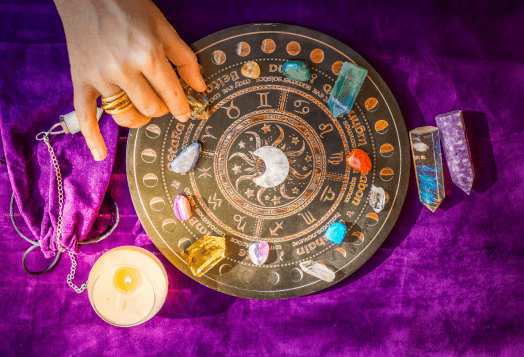 Astrology board with crystals, candle, and pendulum on purple cloth
