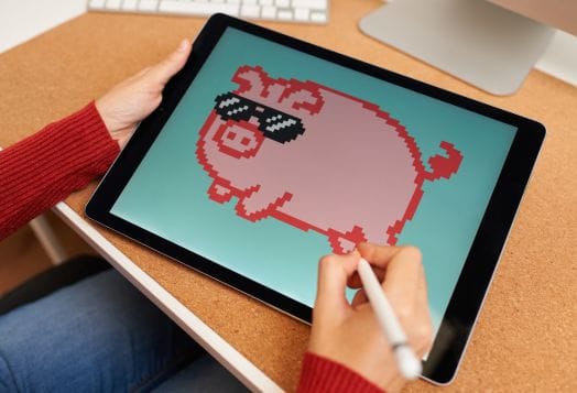 Hands drawing a pixelated pig on a tablet