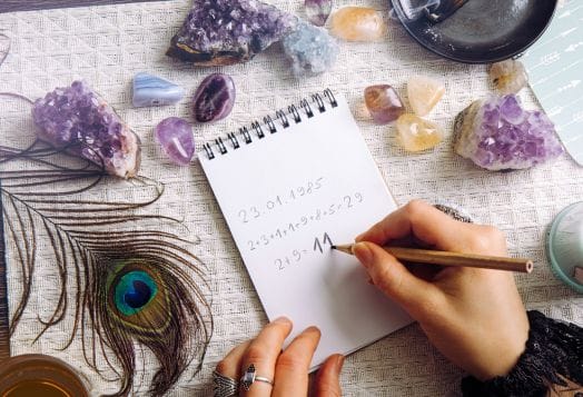 Hands calculating numbers with crystals and feather