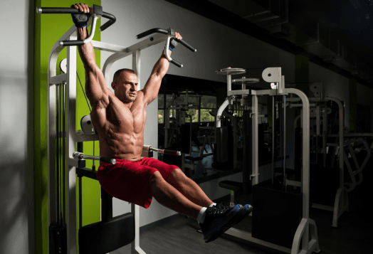 Muscular man doing hanging leg raises at a gym