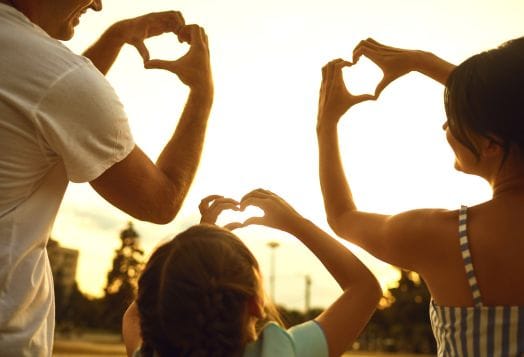 Family making heart shapes with hands at sunset