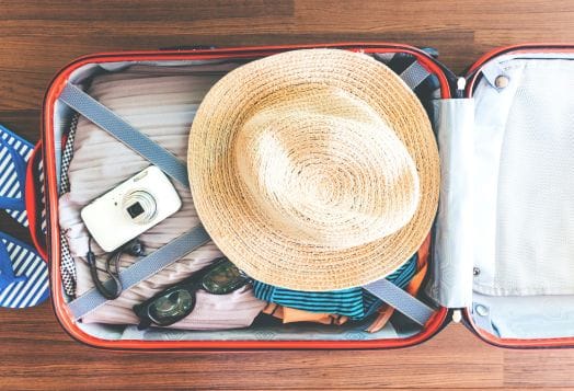 Suitcase packed with hat, camera, and sunglasses