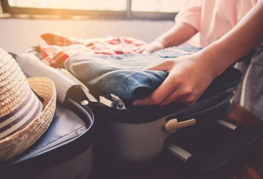 Person packing clothes into suitcase with hat