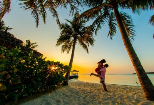 Couple embracing on beach at sunset with palms