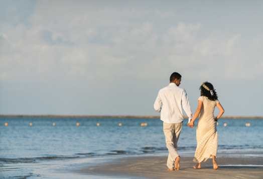 Couple walking hand-in-hand on beach by ocean