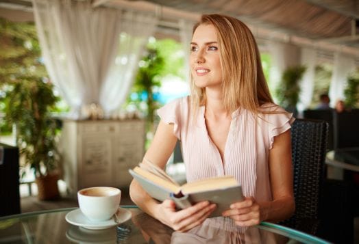 Smiling woman sitting at a café table with a book and a cup of coffee