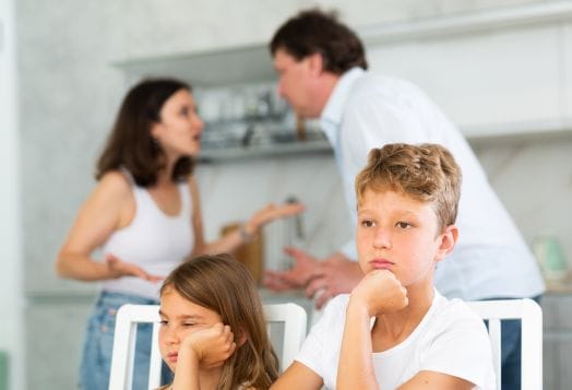 Children looking upset while parents argue in the background