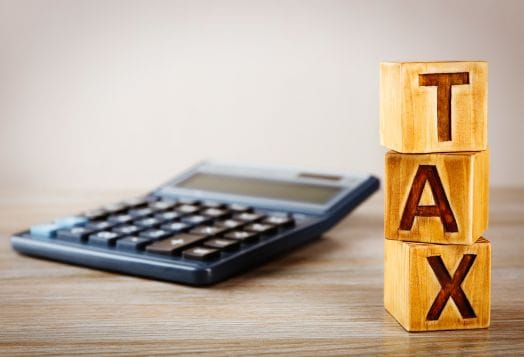 Wooden blocks spelling "TAX" with a calculator