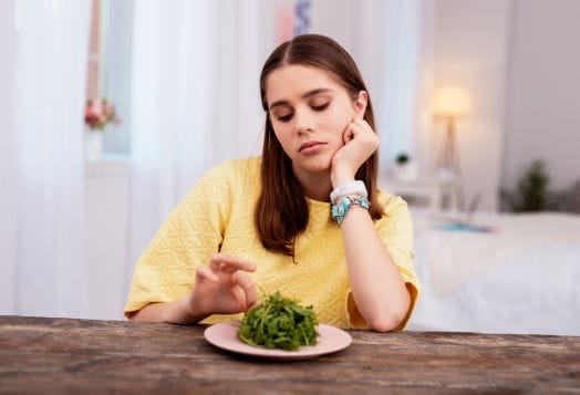 Teenager looking unenthusiastically at a plate of greens