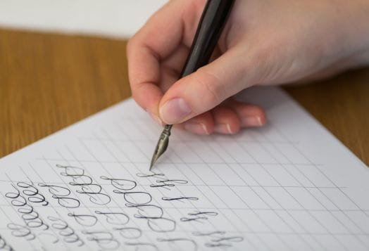 Hand practicing calligraphy with a dip pen
