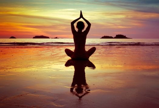 Person practicing desi yoga meditation at sunset on the beach