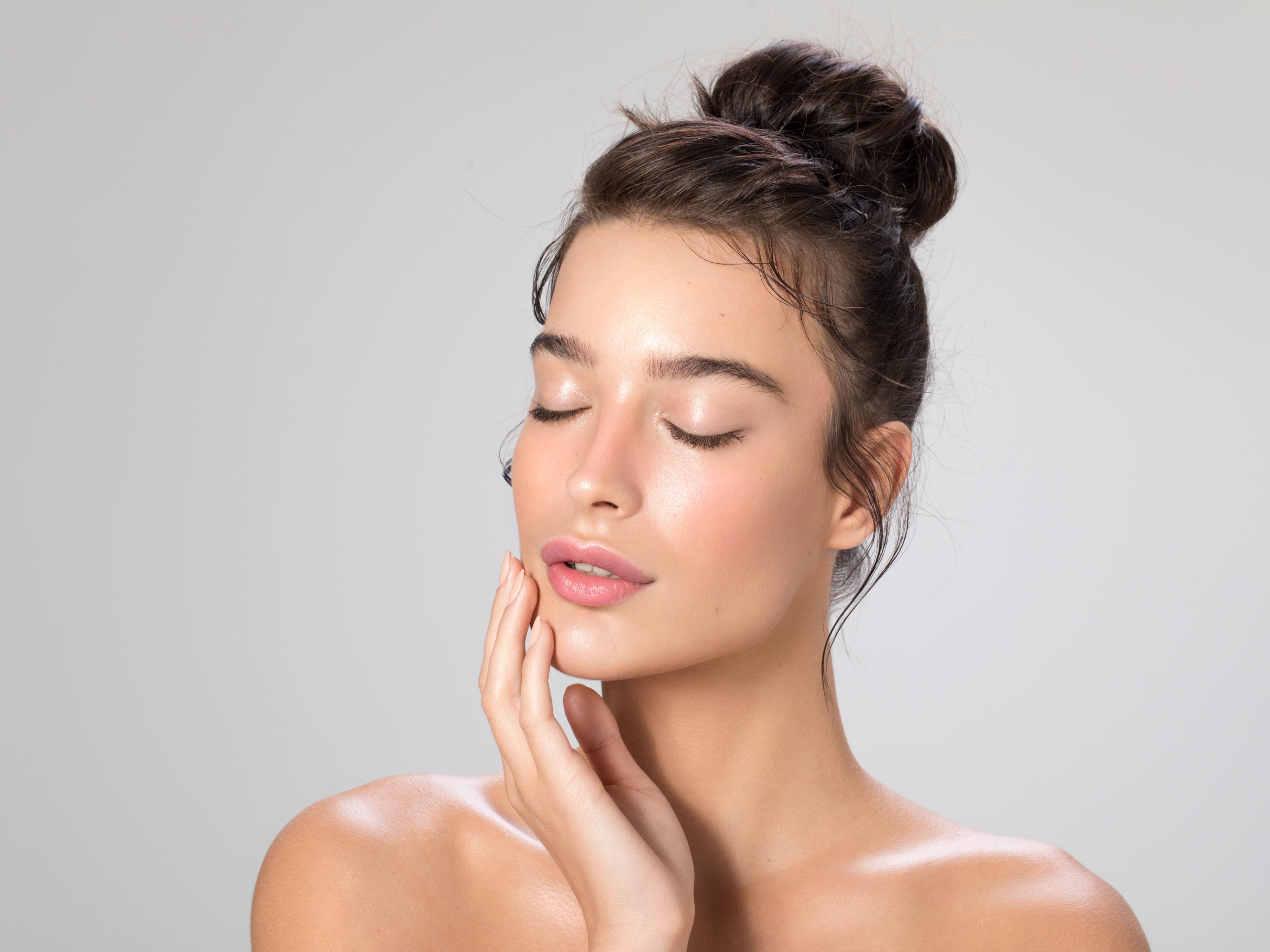 A woman with glowing skin gently touching her face