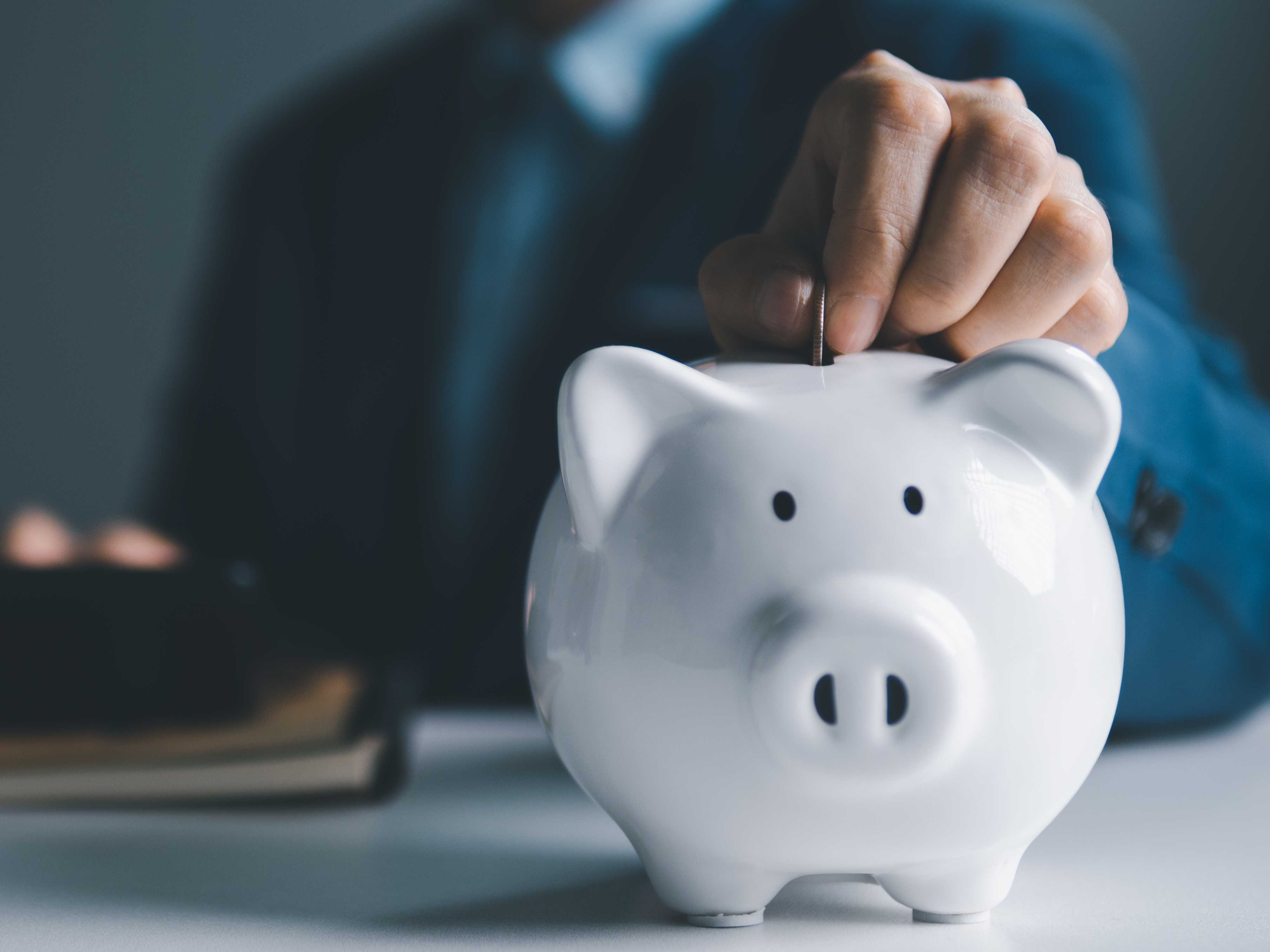 Hand putting money into a piggy bank, symbolizing SIP investment automation