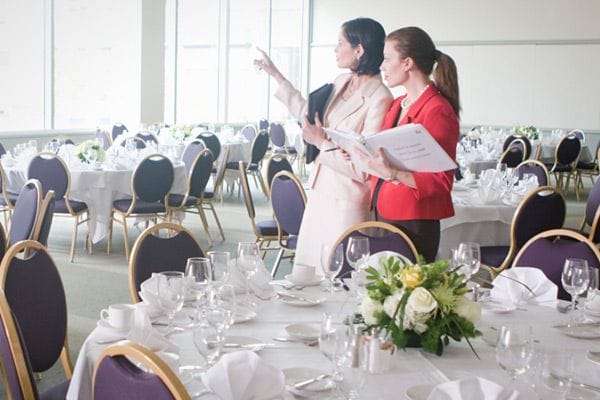 This may contain: two women standing in front of tables with white tablecloths